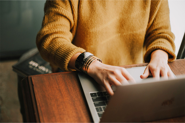 Close up of a person wearing a mustard jumper typing at a laptop 