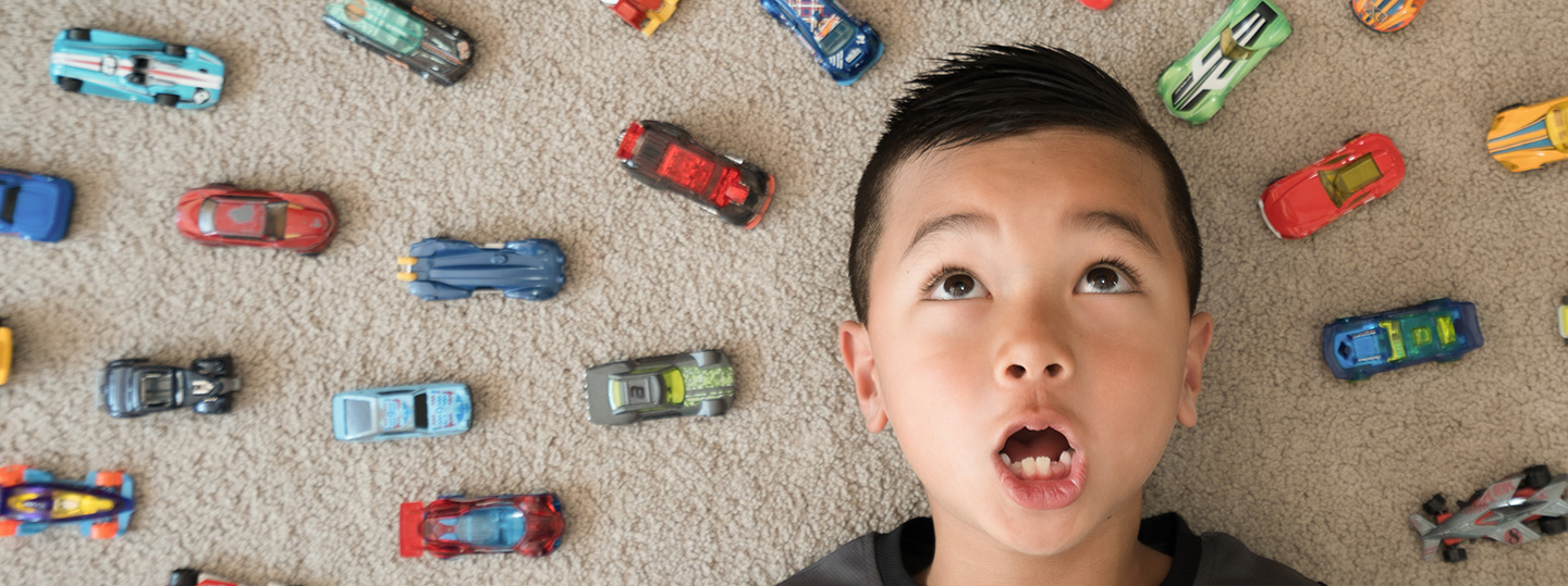 Boy lying on the floor, surrounded by a circle of toy cars