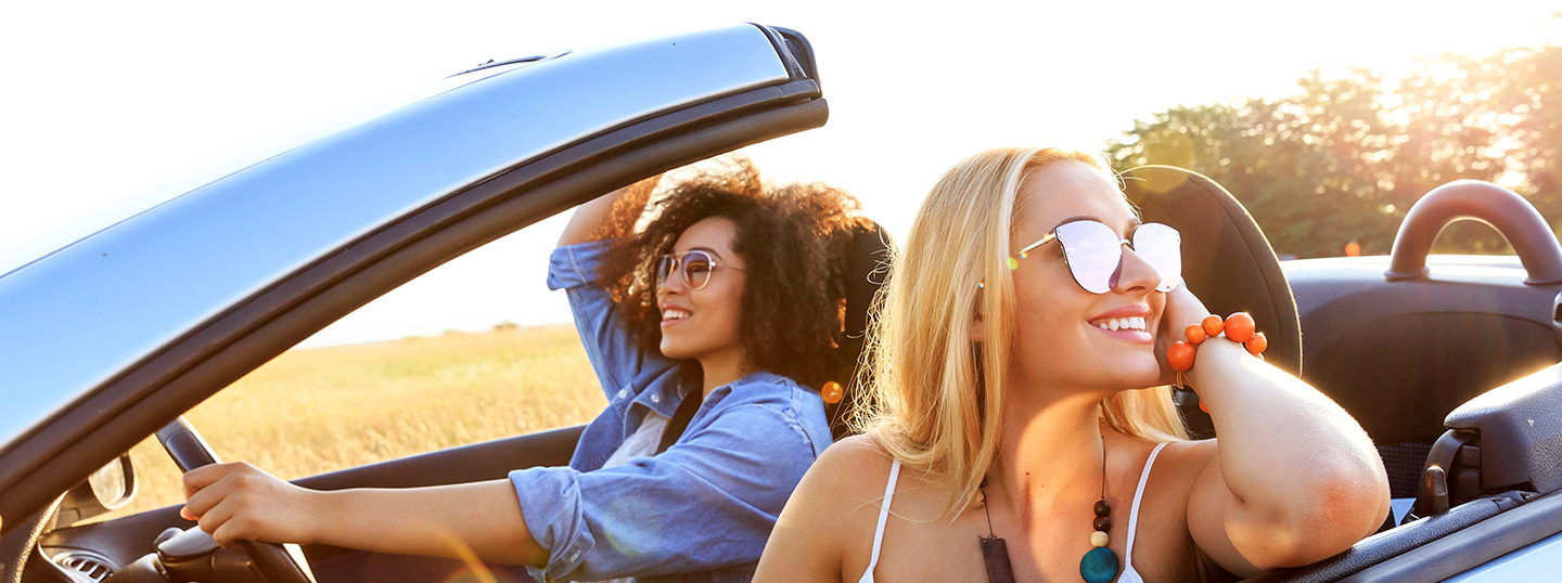 Two women smiling whilst driving in a convertible in the sun