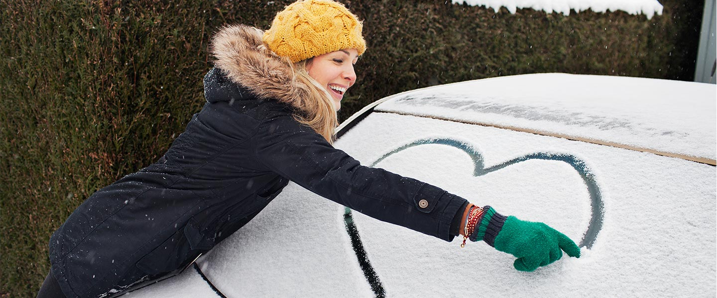 Woman drawing heart out of snow on her car's window