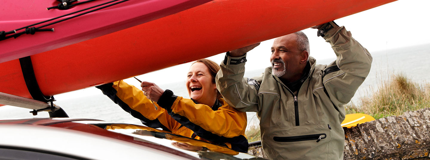 Image of a couple happily fixing a kayak to the top of a car 