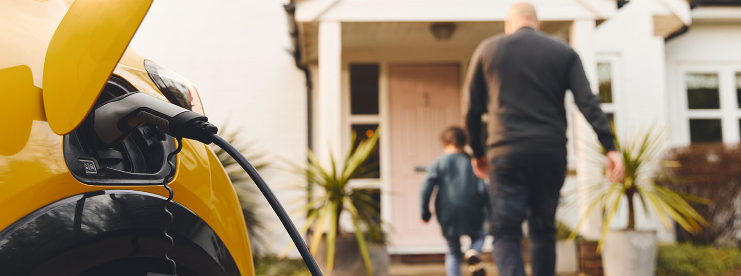 Father and son walking to the front door of their house while the electric car is plugged in to charge