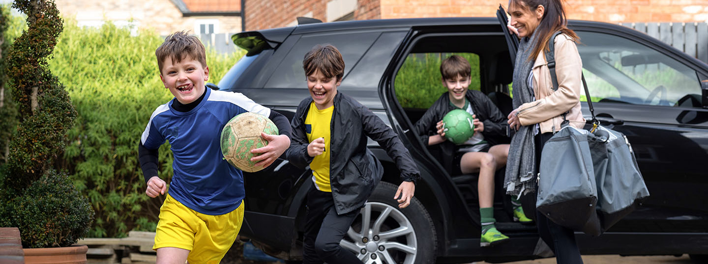 A family getting out of the car, the kids running off to play football together