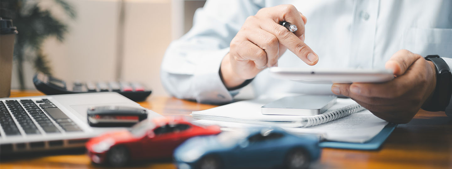 close-up of a person's hands, doing calculations at a professional desk with toy cars in the foreground