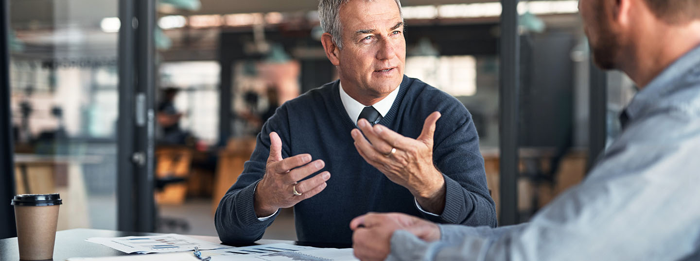 Image of a grey-haired man explaining something passionately to another man in a business setting