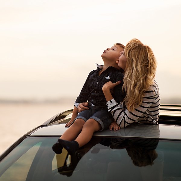 Woman hugging her son, who's sitting on the car's roof, through the sunroof