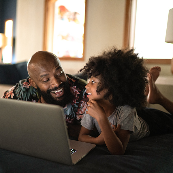 Man laughing and lying on the sofa with his son, looking at a laptop