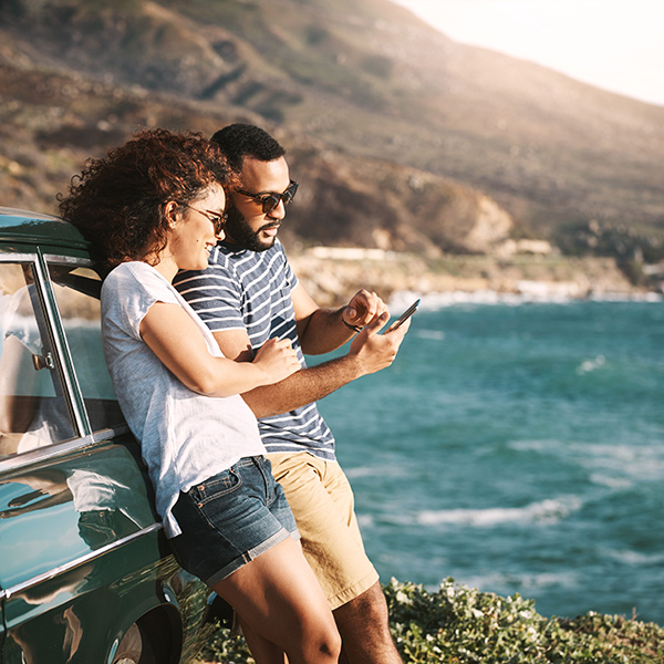 Couple leaning agains their car by the coast, looking at a smartphone