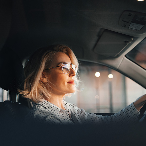 A woman wearing glasses, contentedly driving off in her car 
